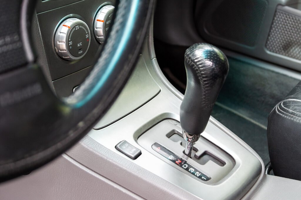 View from the driver's seat of the gear shift lever in a car with an automatic transmission and climate control panel. Black-gray car interior